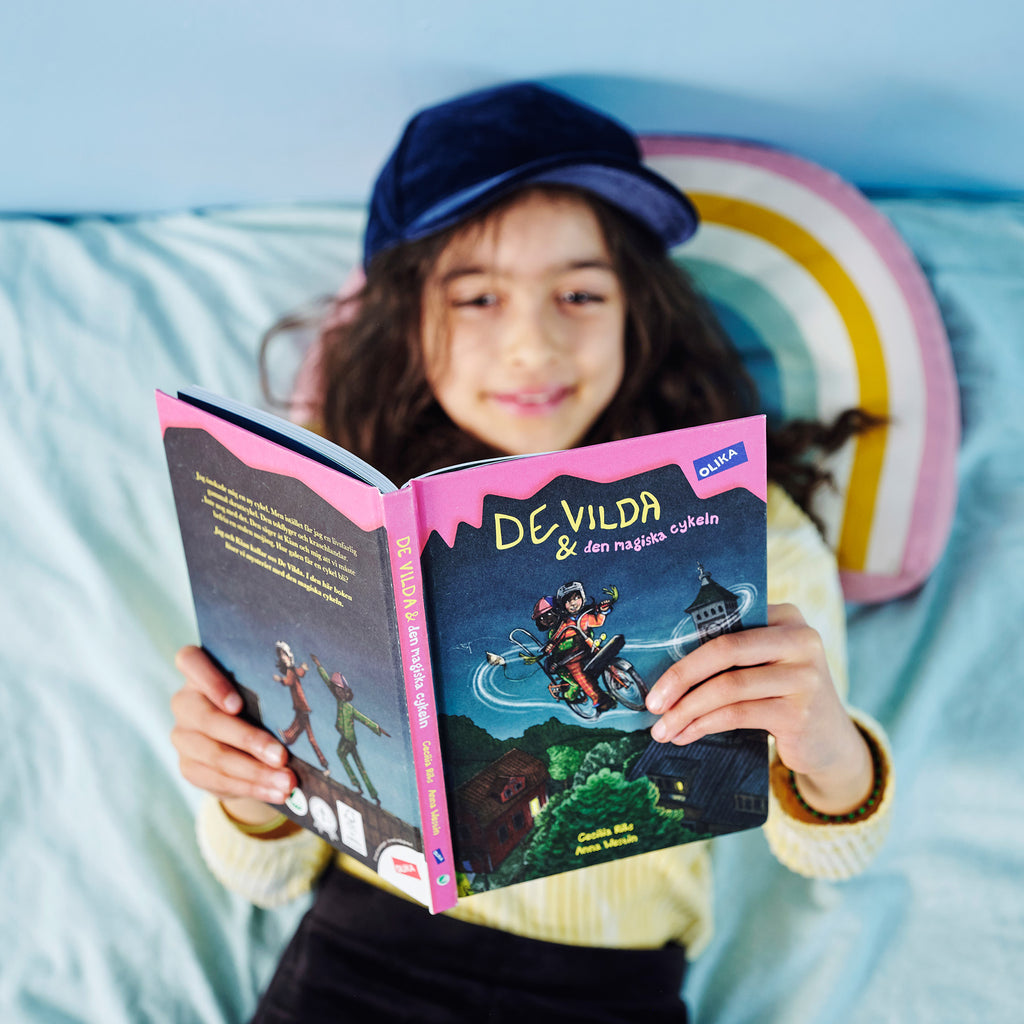 Ett barn ligger i sängen och läser De vilda och den magiska cykeln. 