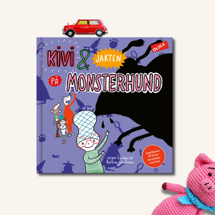 Bilderboken Kivi & jakten på Monsterhund på beige yta. Ovanför boken syns en leksaksbil och i nedre hörnet en virkad gris