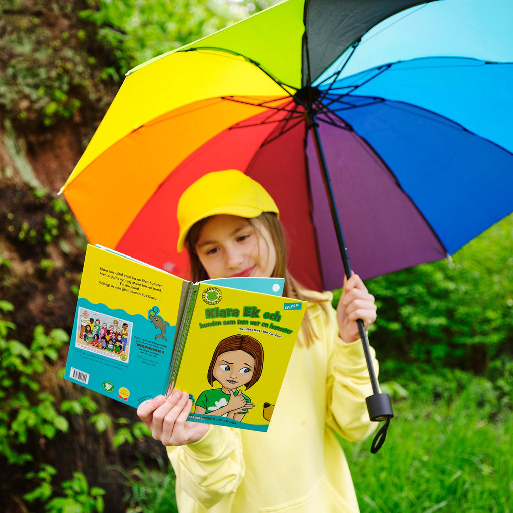 Ett barn med regnbågsparaply läser i Klara Ek & hunden som inte var en hamster -  Barnen i Lyckeskolan - Lättläst 6-9 år  - OLIKA förlag - Författare: Ebba Berg - Illustratör: Carl Flint