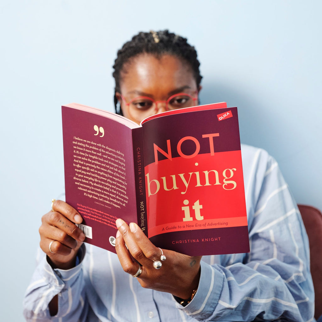 En person sitter inomhus och läser i boken Not buying it - Christina Knight - OLIKA förlag - Författare: Christina Knight - Språk: Engelska