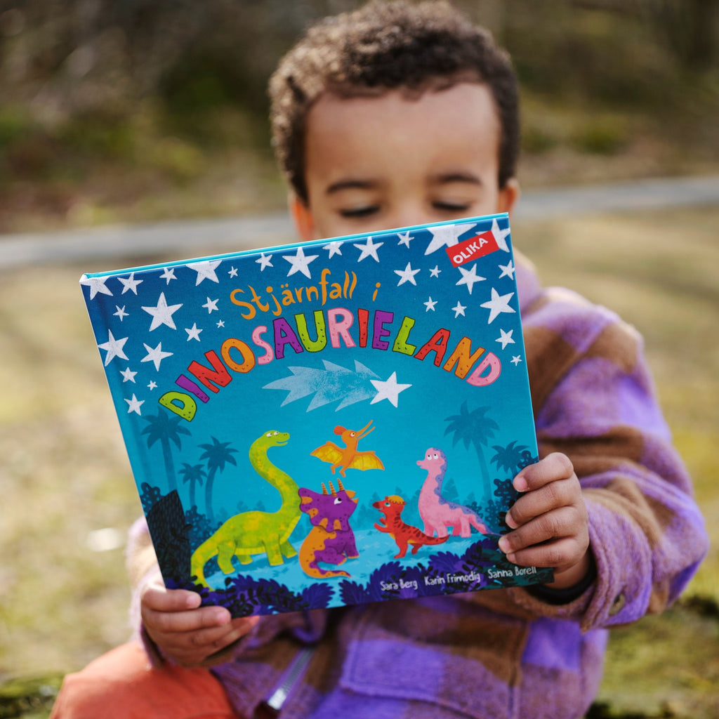 Ett litet barn sitter utomhus och håller upp en kopia av Stjärnfall i dinosaurieland - Bilderbok 3-6 år - OLIKA förlag - Författare: Karin Frimodig och Sara Berg - Illustratör: Sanna Borell