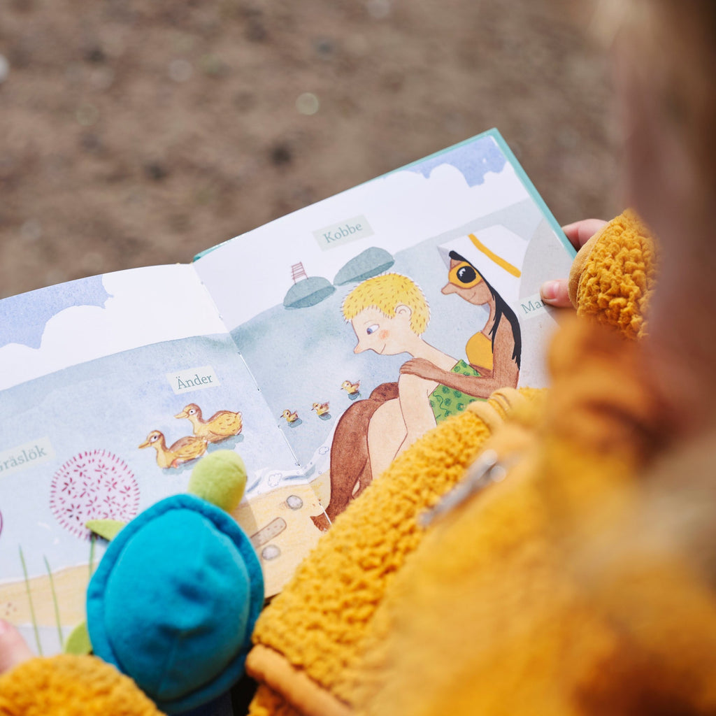Ett barn i gul tröja tittar ner på en illustrerad strand i Titta havet! - Bilderbok 0-2 år - OLIKA förlag - Författare: Åsa Mendel-Hartvig - Illustratör: Maija Hurme