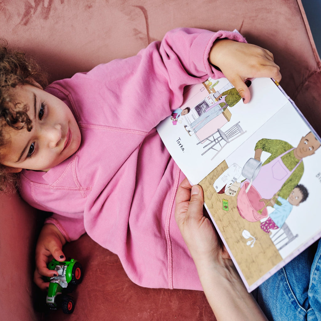 Ett barn leker med en bil och håller i en kopia av Vi bakar bullar - Bilderbok 1-3 år - OLIKA förlag - Författare: Sarah Vegna - Illustratör: Astrid Tolke