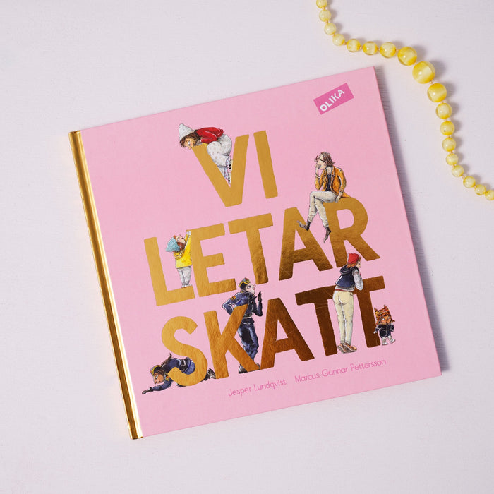 Bilderboken Vi letar skatt på vit yta. I övre högra hörnet syns ett gult pärlhalsband