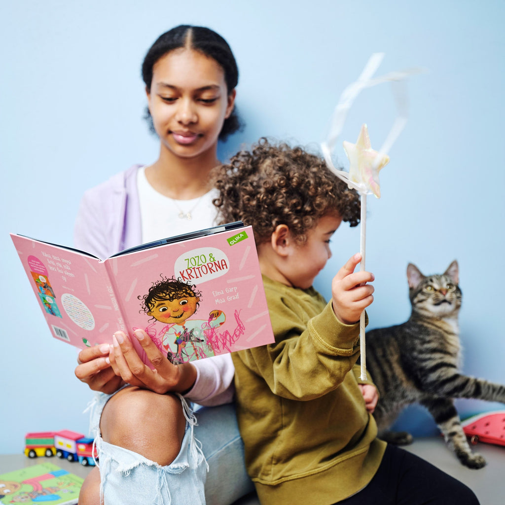 En ungdom sitter inomhus tillsammans med ett barn och en katt och läser Zozo och kritorna - Bilderbok 1-3 år - OLIKA förlag - Författare: Elina Garp - Illustratör: Moa Graaf