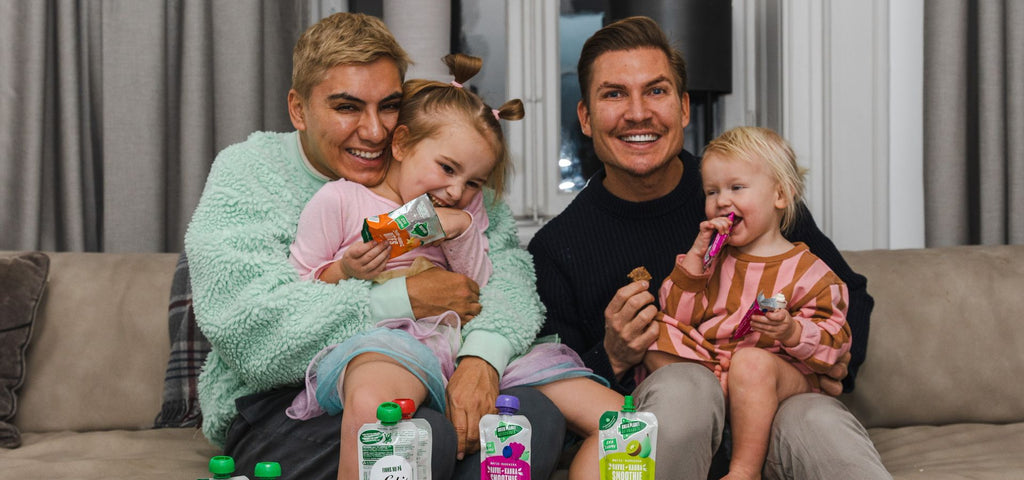 Färgfoto av Johan och John Valencia med sina två barn Miriam och Astrid i knät. De sitter i en soffa och barnen äter snacks
