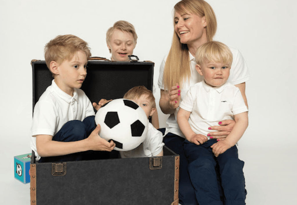 Ett färgfoto av Kind Emily med sina fyra barn, två av barnen sitter i en kista med leksaker, en av dem håller i en fotboll