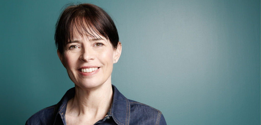 Färgfoto av författaren Christina Knight som står mot en blå vägg och ler mot kameran