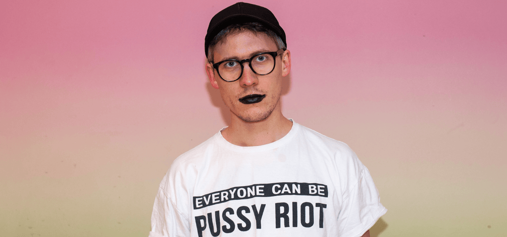 Färgfoto av Makz Bjuggfält som står mot rosa bakgrund och ser in i kameran