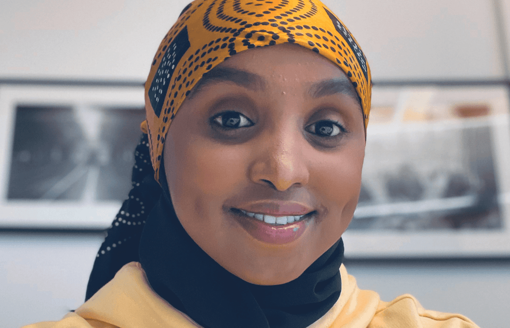 Färgfoto av Muna Idow som befinner sig inomhus och ler mot kameran
