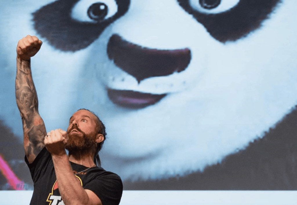 Färgfoto av föreläsaren Peter Rung som står framför ett foto av Po från filmen Kung Fu Panda. Peter håller upp ena knytnäven
