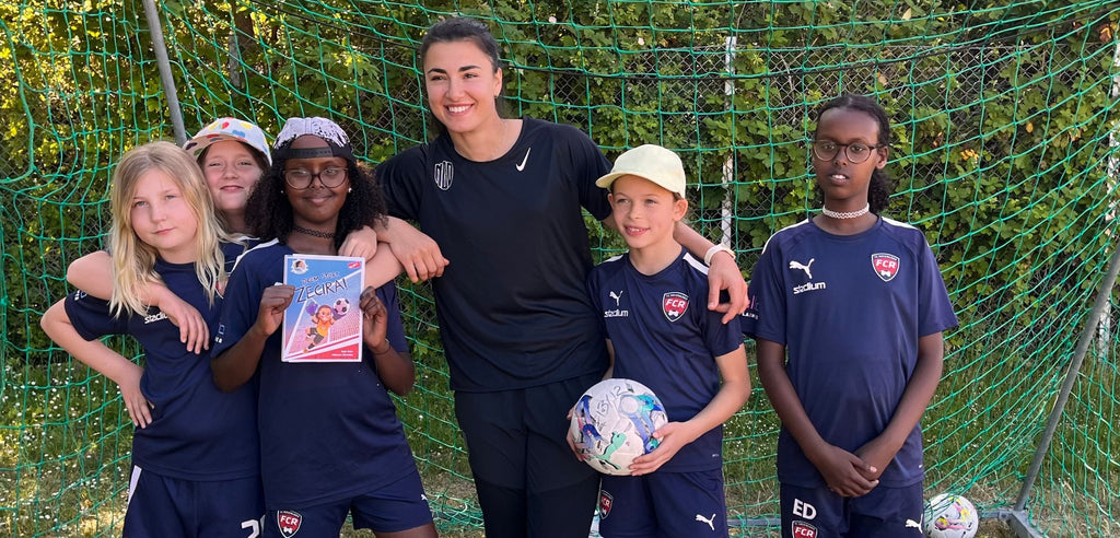 Färgfoto av ett barnfotbollslag tillsammans med Zećira Mušović, ett av barnen håller i boken Dröm stort, Zećira!