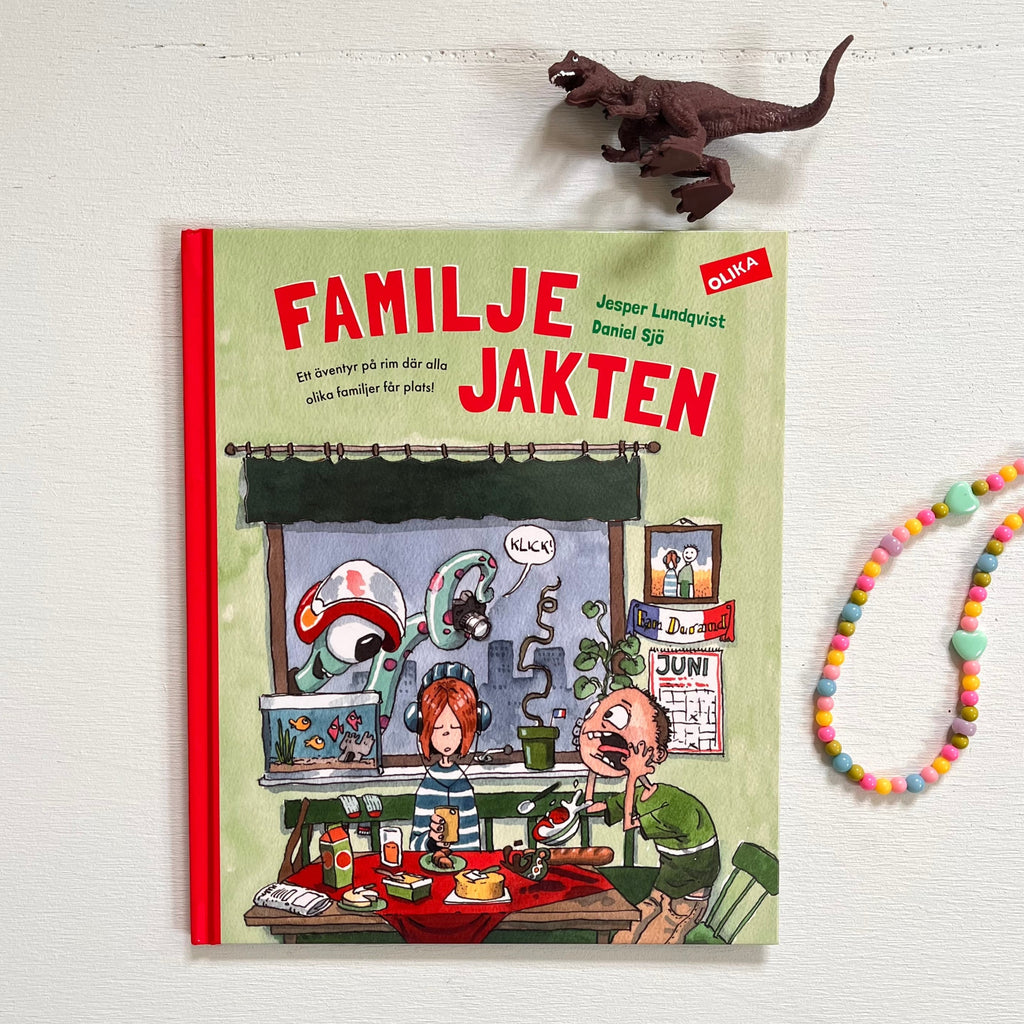 Omslaget till Familjejakten fotat med en dinosaurie och ett halsband bredvid - Familjejakten - Bilderbok 3-6 år - OLIKA förlag - Författare: Jesper Lundqvist - Illustratör: Daniel Sjö