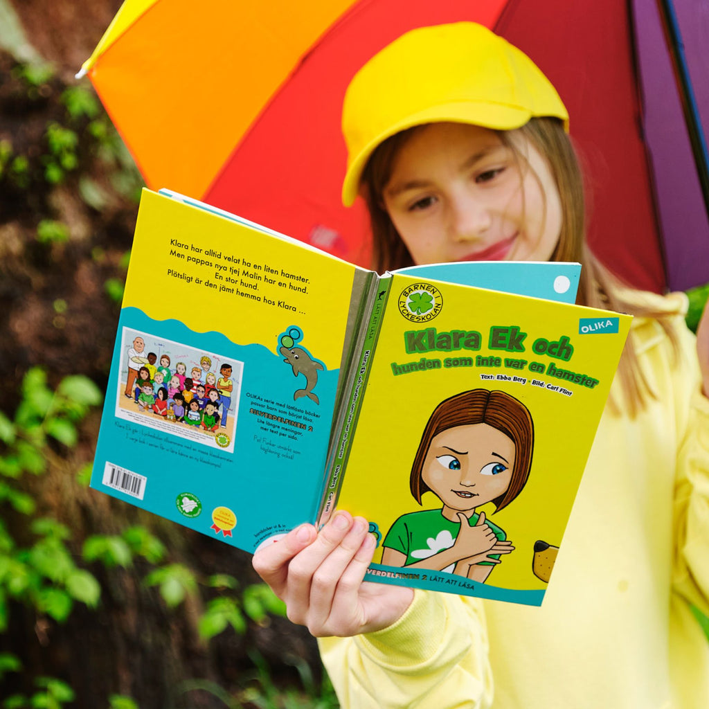 Ett barn som håller i ett regnbågsparaply läser Klara Ek och hunden som inte var en hamster.