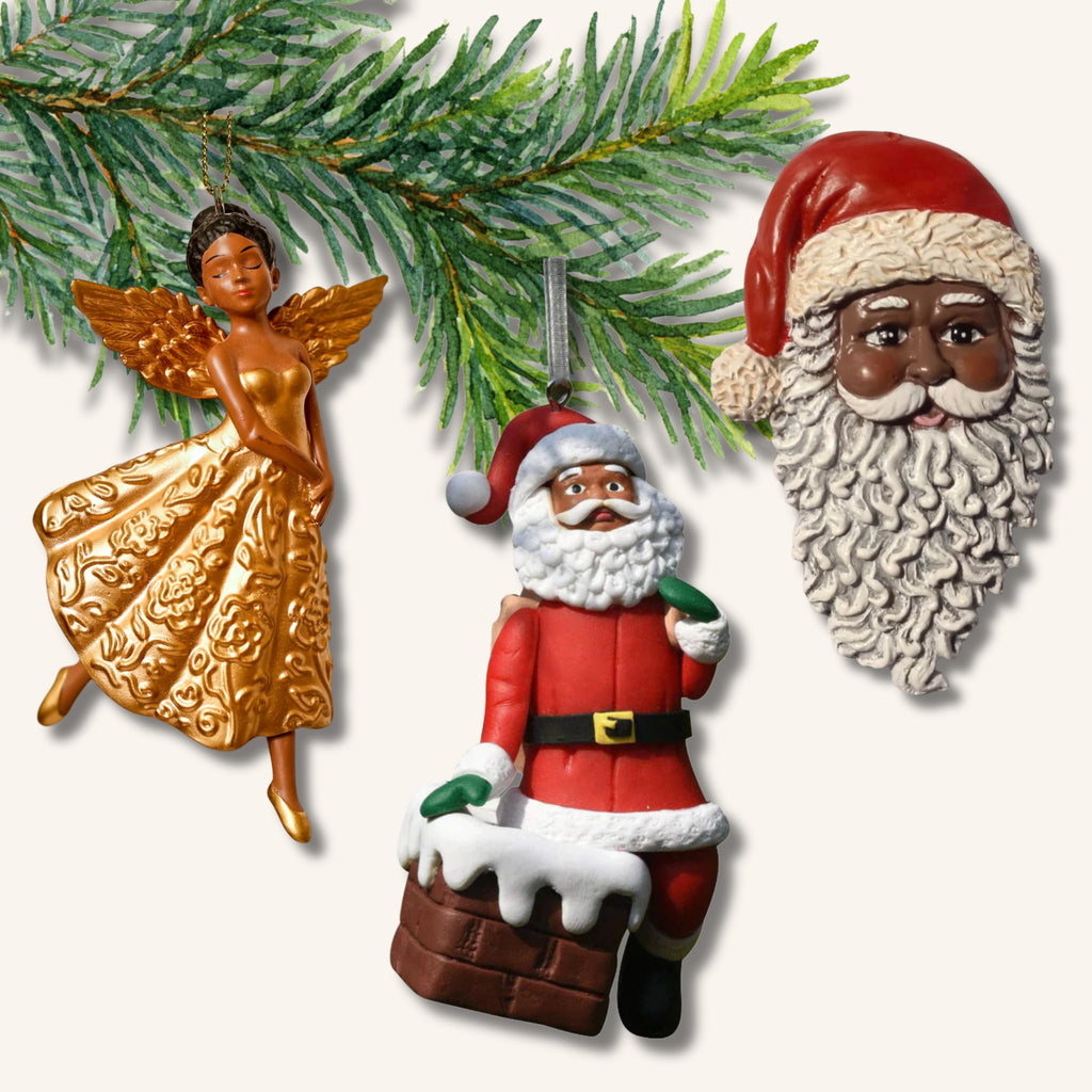 Tre juldekorationer föreställande tomtar och en ängel med brun hudfärg, hänger på en grankvist.