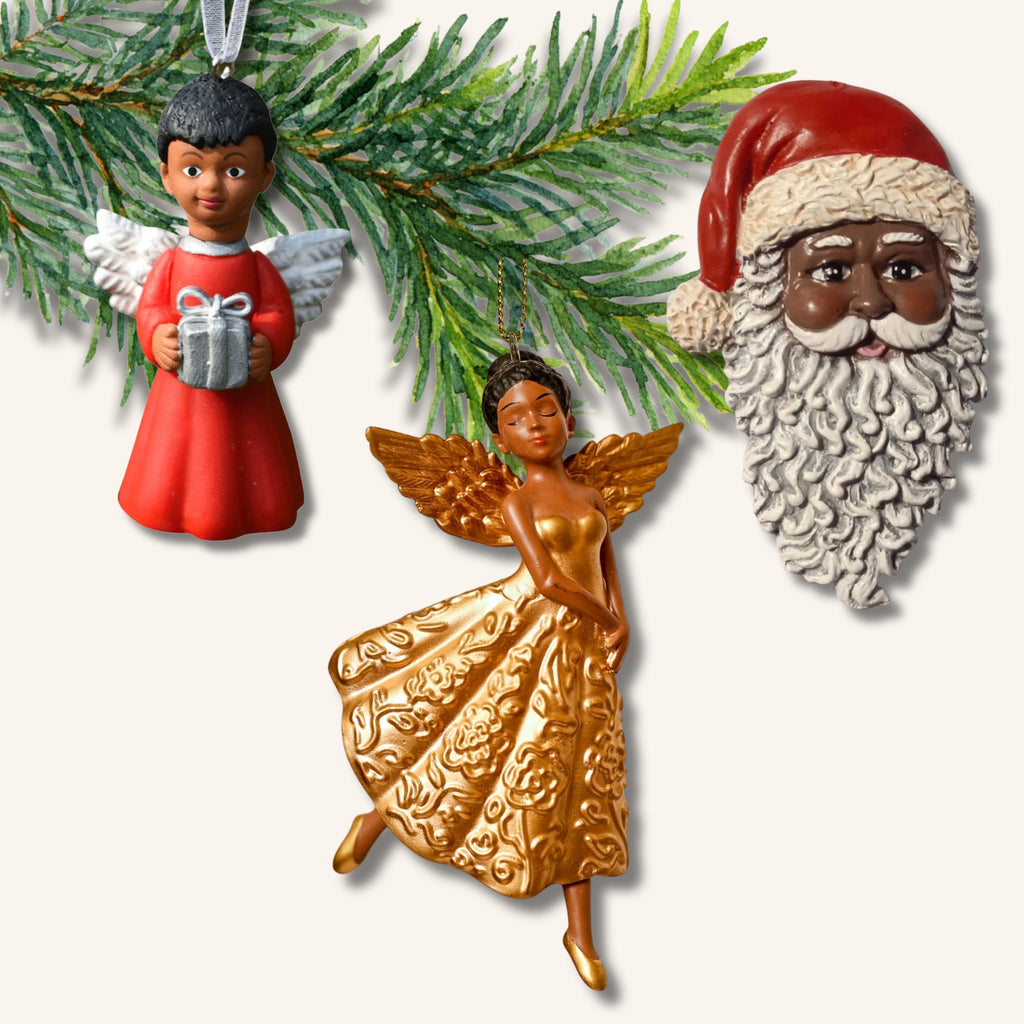 Tre juldekorationer föreställande tomte och änglar med brun hudfärg, hänger på en grankvist.