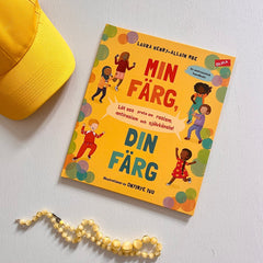 Metodboken Din färg, min färg på träyta. Bredvid syns en gul keps och nedanför ett gult pärlhalsband