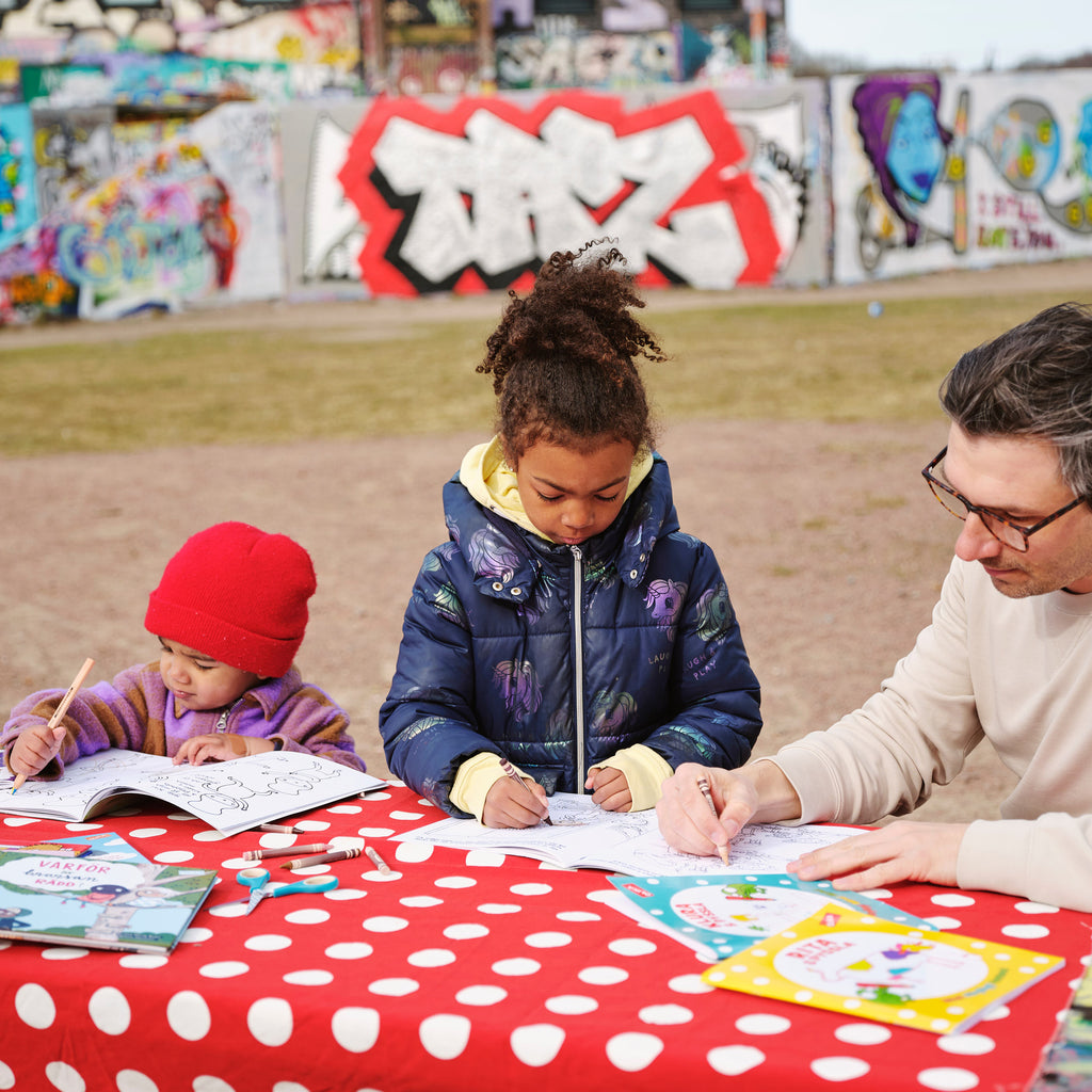 Två förskolebarn som ritar och pysslar utomhus tillsammans med en pedagog