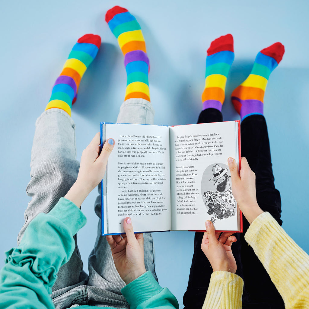 Bild tagen uppifrån. Man ser händer och ben och av två barn som håller i en bok och läser.