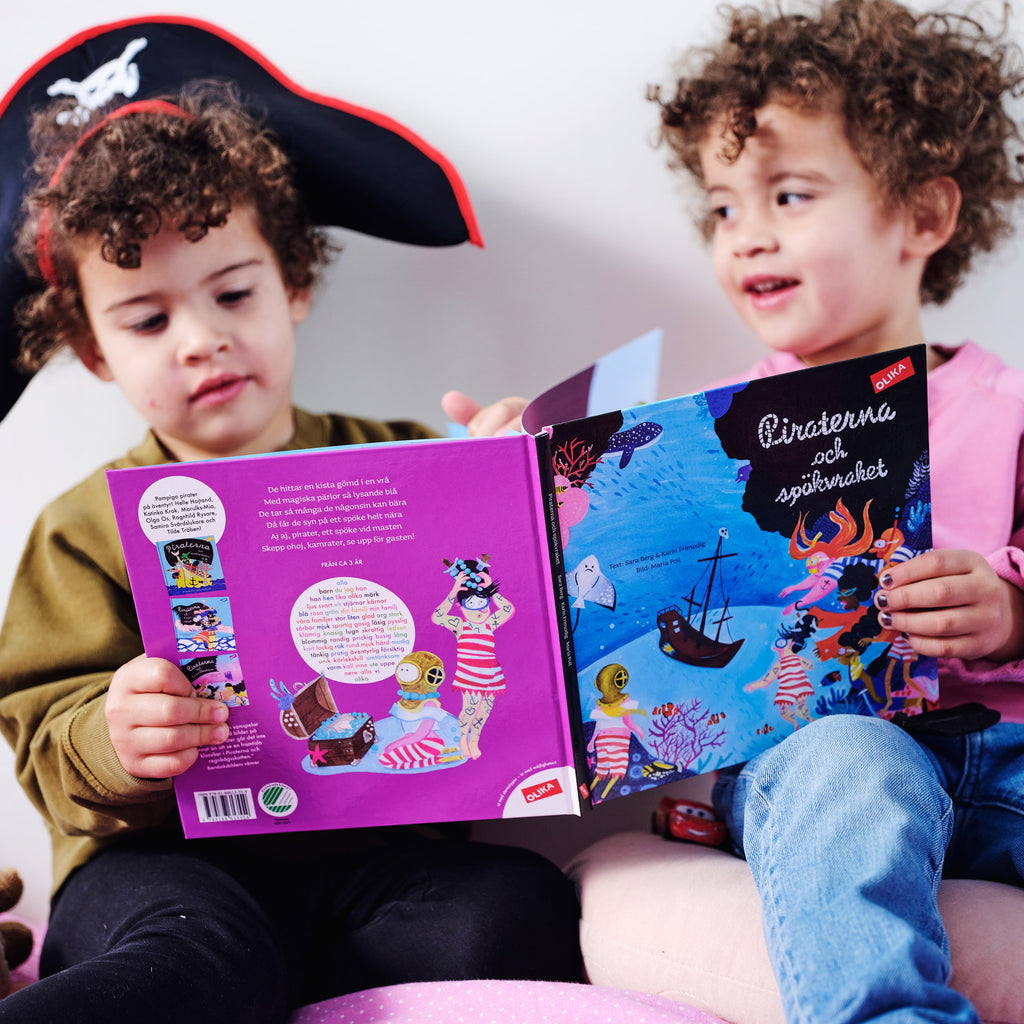 Två barn läser Piraterna och spökvraket. Det ena barnet har en pirathatt på sig. 