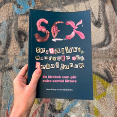 Någon håller upp metodboken SEX, sexualitet, samtycke och relationer mot en vägg full av graffitti 