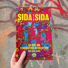 Någon håller upp metodboken Sida vid sida mot en vägg full av graffitti