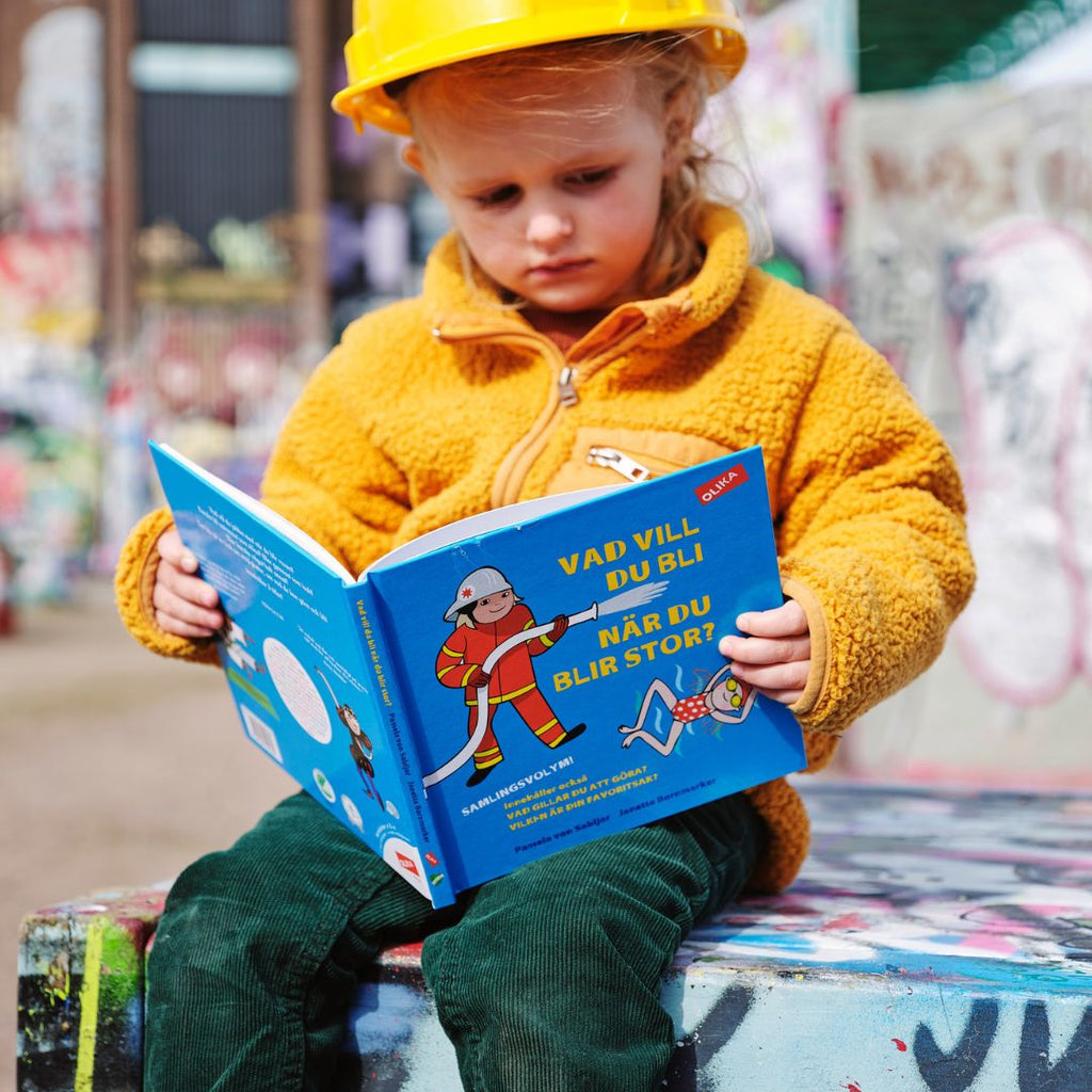 Ett barn med bygghjälm på huvudet läser Vad vill du bli när du blir stor?