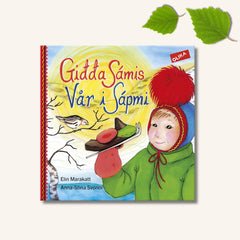 Omslaget till barnboken Vår i Sápmi går i samiska färger.  Ett barn med samiska kläder leker i snön. 
