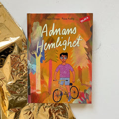 Kapitelboken Adnans hemlighet ligger delvis på vit träyta, delvis på presentpapper i guld
