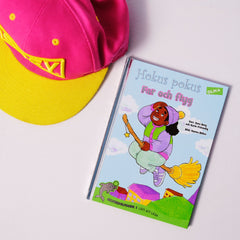 Lätt att läsa boken Hokus pokus: Far och flyg syns på vit yta med en rosa keps med gula detaljer