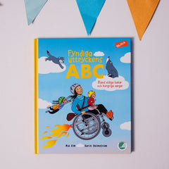 Bilderboken Fyndiga uttryckens ABC syns på vit yta, ovanför syns en färgglad vimpelgirlang