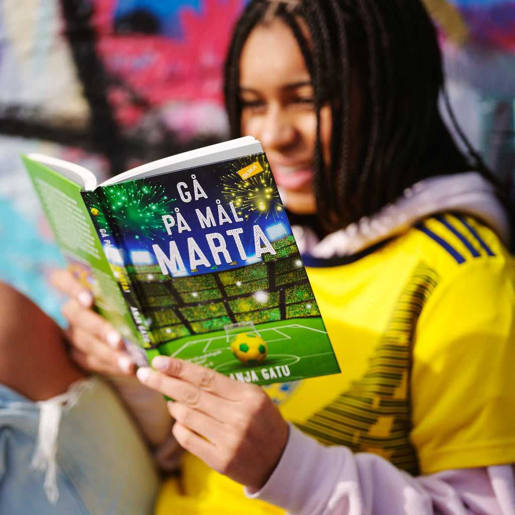 En person håller upp boken Gå på mål, Marta - Kapitelbok 9-12 år - OLIKA förlag - Baserad på fotbollsstjärnan Marta Vieira da Silvas barndom - Författare: Anja Gatu
