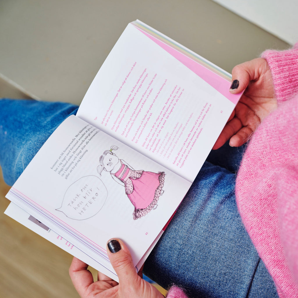 En vuxen i rosa tröja visar en illustration av en rosaklädd karaktär i boken Ge ditt barn 100 möjligheter istället för 2 - OLIKA förlag - Författare: Kristina Henkel och Marie Tomičić - Illustratör: Emili Kvarnström Svensson