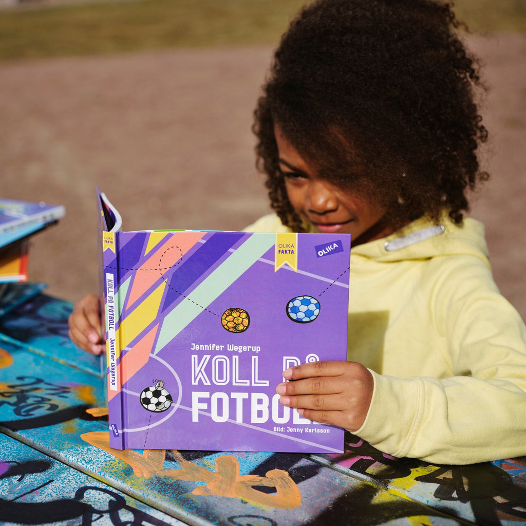 Ett barn sitter utomhus och läser i Koll på fotboll - Faktabok 5 - 100 år - OLIKA förlag - Författare: Jennifer Wegerup - Illustratör: Jenny Karlsson