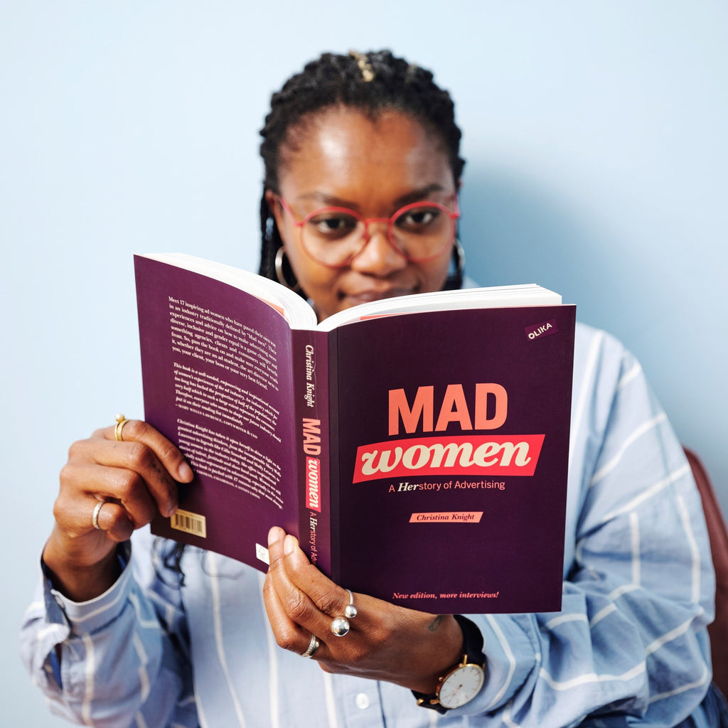 En person klädd i randig skjorta läser i boken Mad women - A herstory of advertising - OLIKA förlag - Författare: Christina Knight - Språk: Engelska