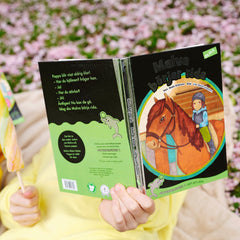 Ett barn i gul tröja ligger på en filt, äter glass och läser lätt att läsa boken Malva börjar rida. I gräset syns blommor