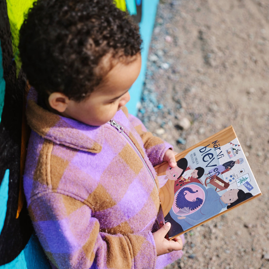 Ett barn står utomhus och håller i en kopia av När vi blev en till - Bilderbok 1-3 år - OLIKA förlag - Författare: Anna Lundgren - Illustratör: Mia Olofsson