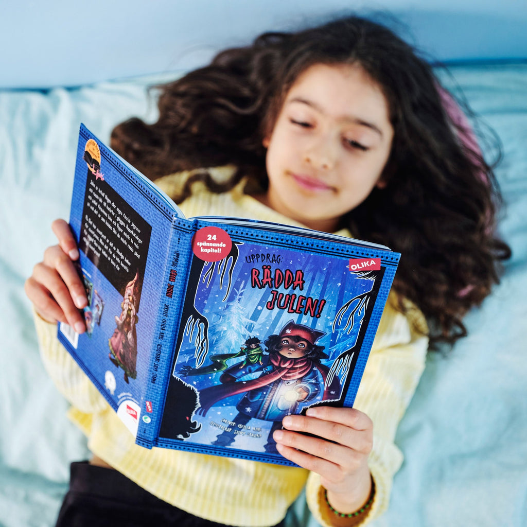 Ett barn ligger på en säng och läser i Uppdrag: Rädda julen - Kapitelbok 6-9 år - OLIKA förlag - Författare: Cecilia Rihs - Illustratör: Silvy Strand