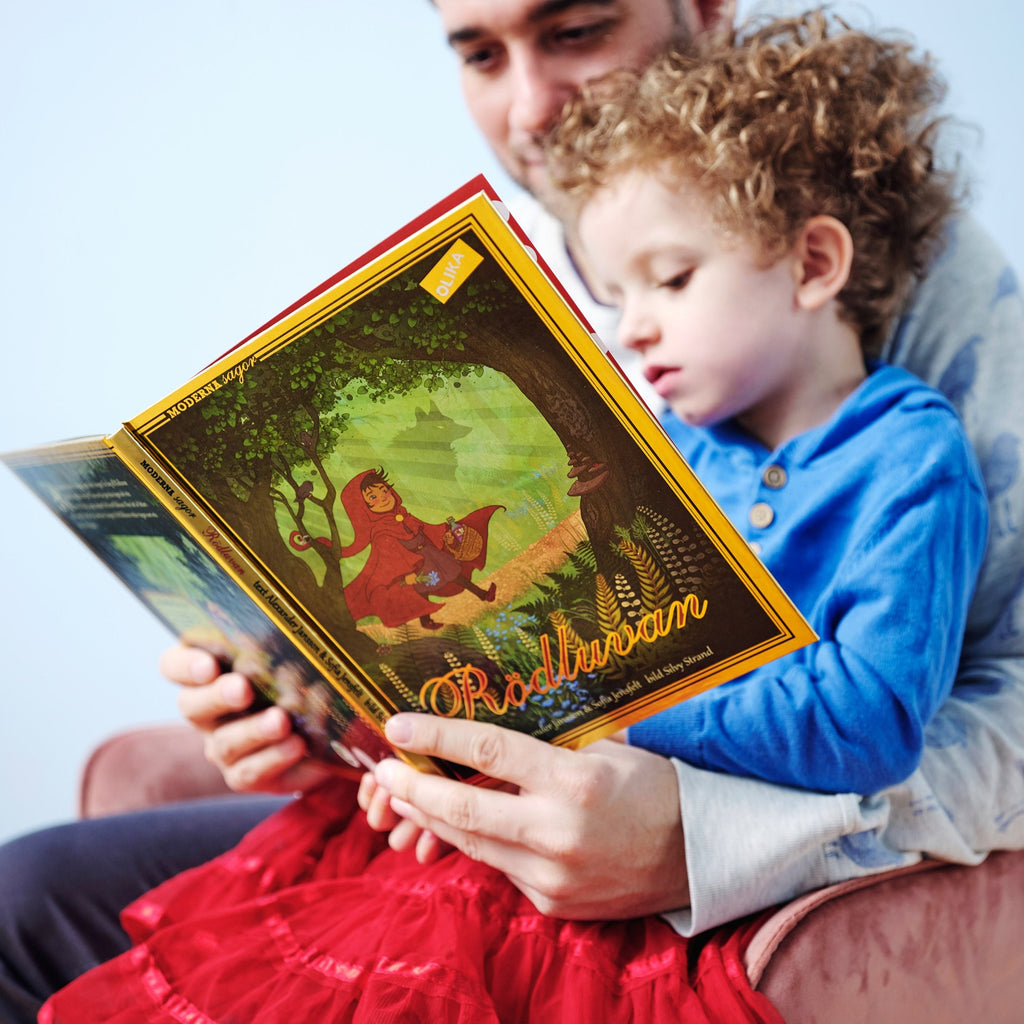 En vuxen och ett barn klädd i röd kjol läser tillsammans i Rödluvan - Bilderbok 3-6 år - OLIKA förlag - Författare: Alexander Jansson, Sofia Jensfelt Illustratör: Silvy Strand