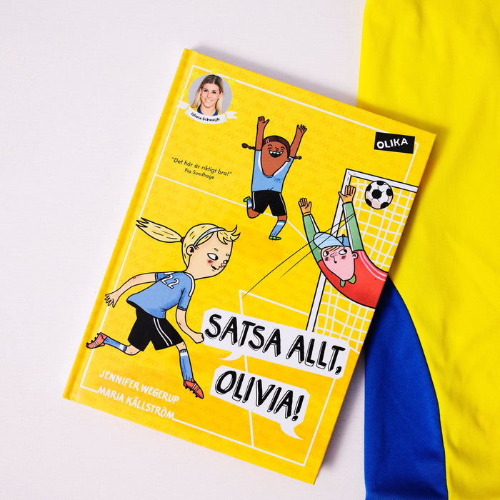 Kapitelboken Satsa allt, Olivia! ligger delvis på vit yta, delvis ovanpå en blågul fotbollströja