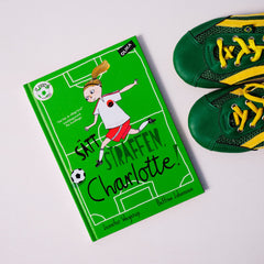 Kapitelboken Sätt straffen, Charlotte! syns på vit yta tillsammans med ett par gröna fotbollsskor med gula snören