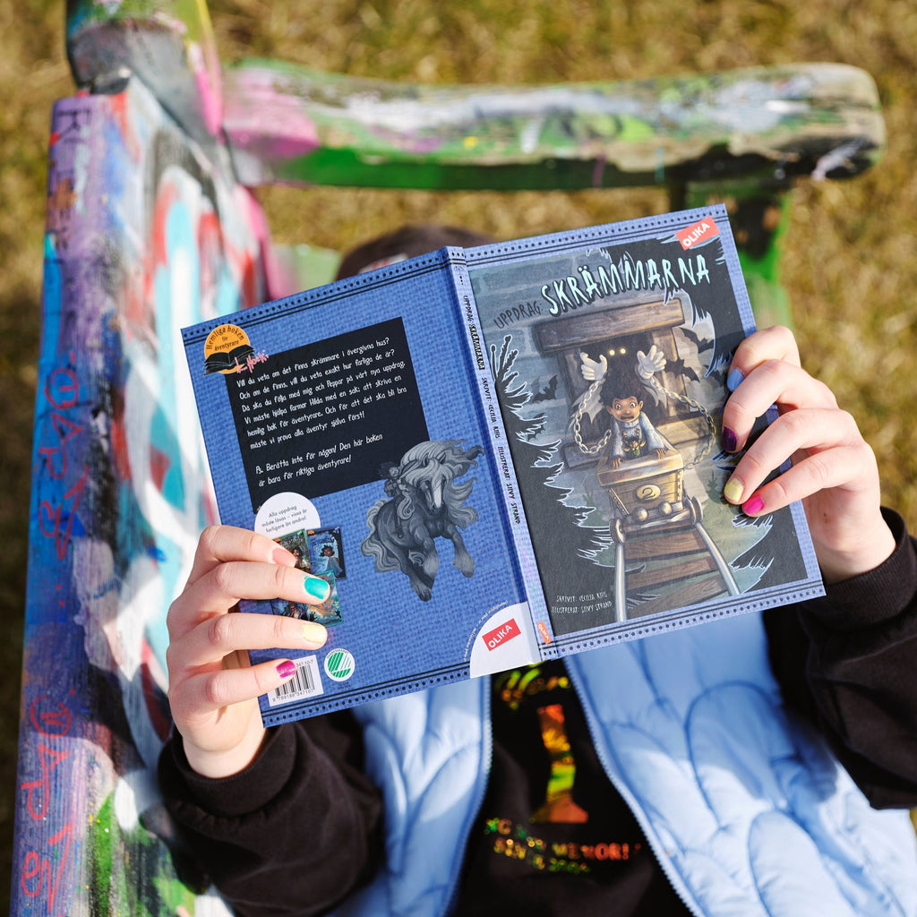 Ett barn ligger utomhus på en parkbänk och läser Uppdrag: Skrämmarna - Kapitelbok 6-9 år - OLIKA förlag - Författare: Cecilia Rihs - Illustratör: Silvy Strand