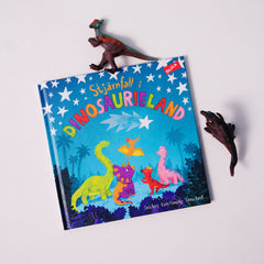 En bilderbok om dinosaurier ligger på vit yta tillsammans med två plastdinosaurier.