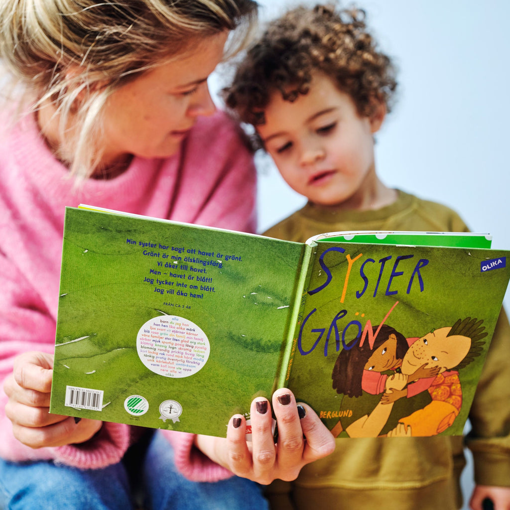 Ett barn och en vuxen bläddrar i ett exemplar av Syster grön av Jessika Berglund