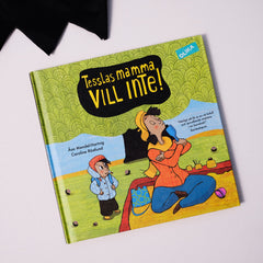 Bilderboken Tesslas mamma vill inte! syns på vit yta med en bit svart tyg