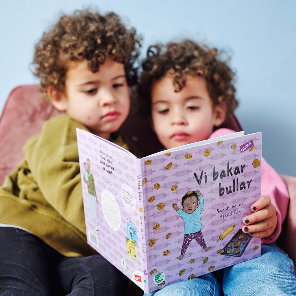 Två barn med lockigt hår läser tillsammans i Vi bakar bullar - Bilderbok 1-3 år - OLIKA förlag - Författare: Sarah Vegna - Illustratör: Astrid Tolke